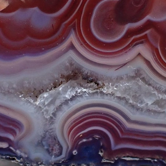 close-up of malawi agate with flow channel and fortification banding in deep reds, crystalline centre