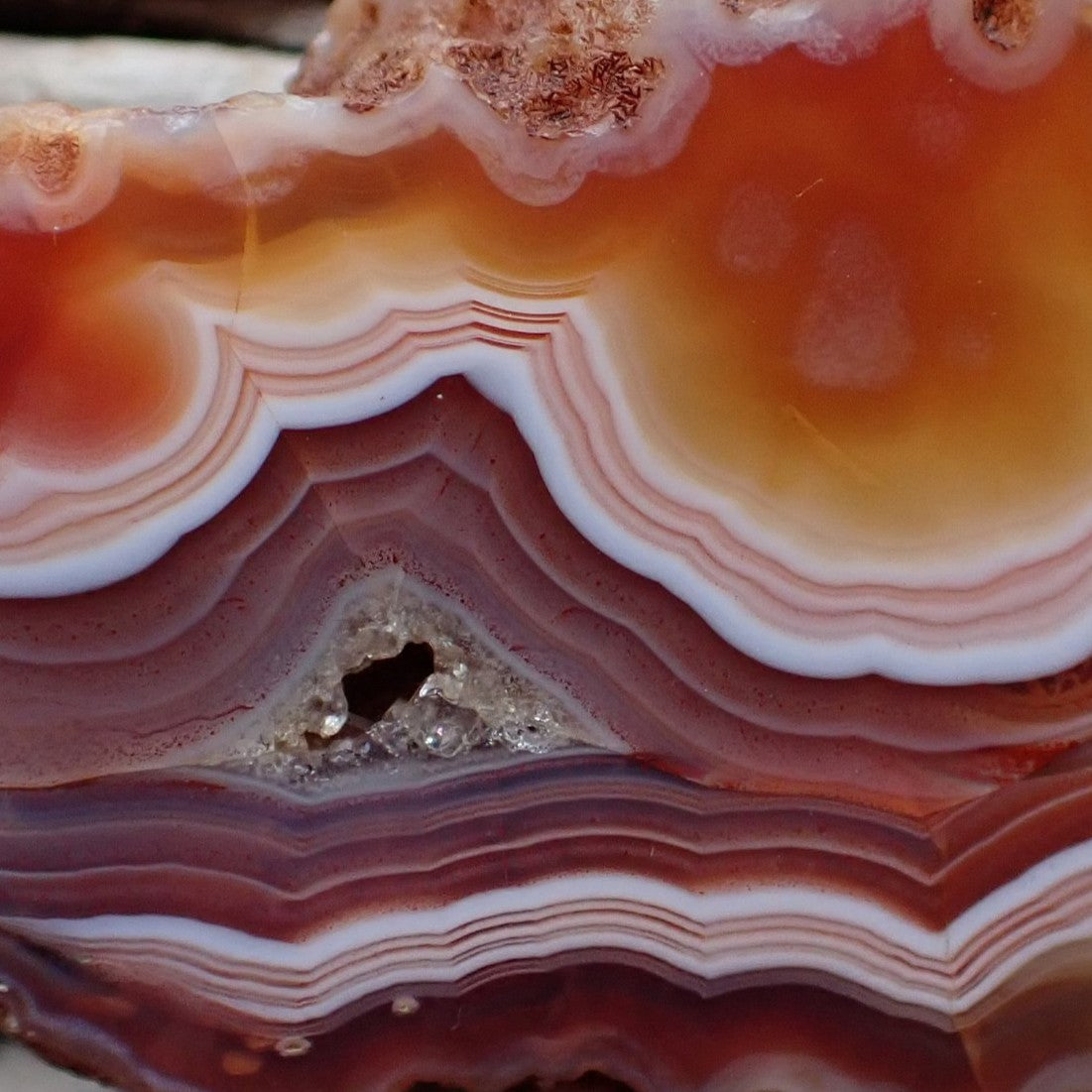 Close-up of Malawi agate 51 mm – dual fortification banding convergence, flow channel, triangular micro-crystalline vug and warm carnelian-amber to sard-red palette detail | SKU 000354
