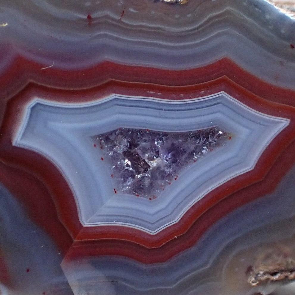 Close-up of a Malawi candy agate with reds and grey blues surrounding a druy amethyst centre