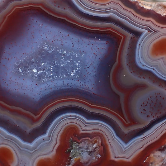 Close-up of a Malawi candy agate crystalline centre surrounded in purple and red peach and orange banding
