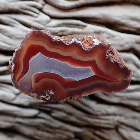 Polished malawi agate with red and salmon peach banding with a crystalline centre exiting in a flow channel