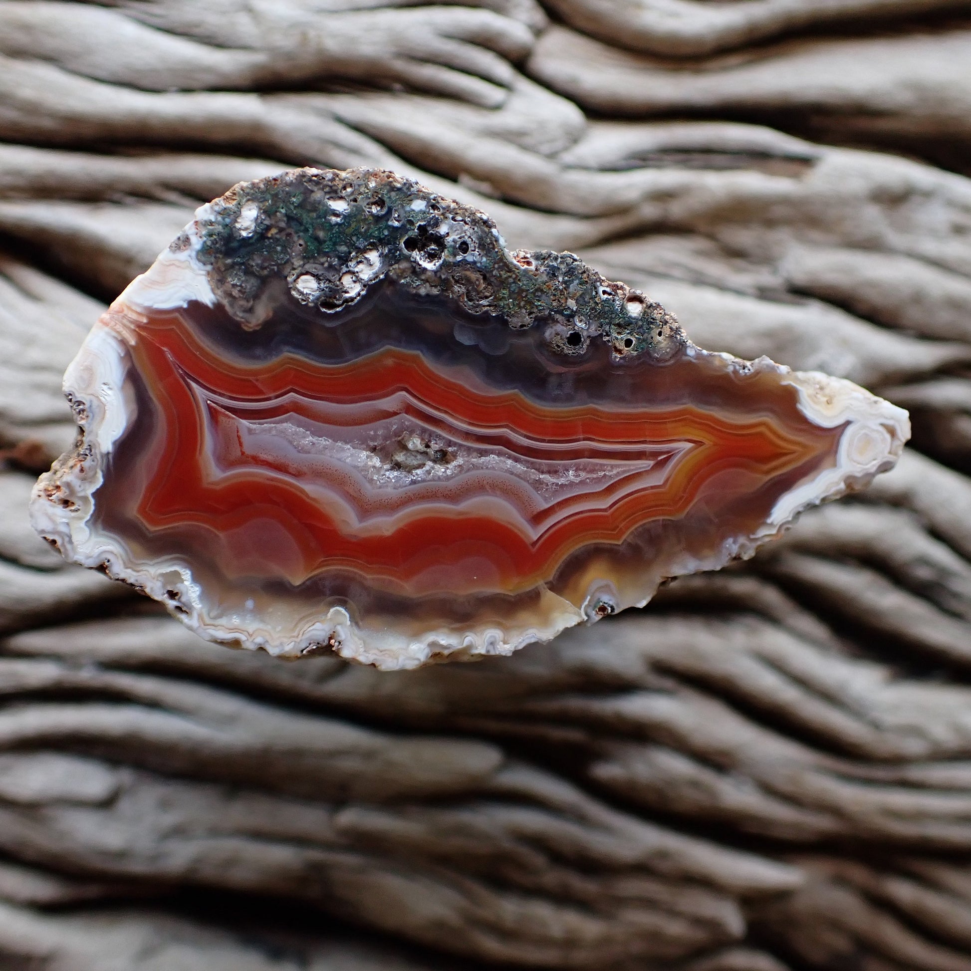 Polished Malawi agate with ghost banding on the outer rim going into vibrant red and orange banding surrounding a spearlking crystalline centre