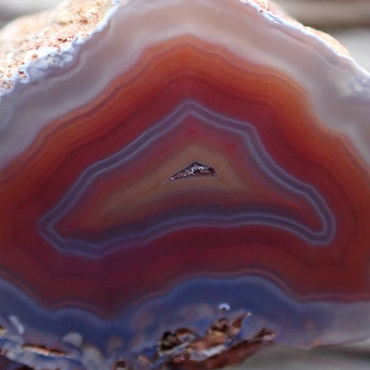 Close-up of a multicolored Malawi Ngabu agate stone with concentric layers of red, orange and a faint purple/blue