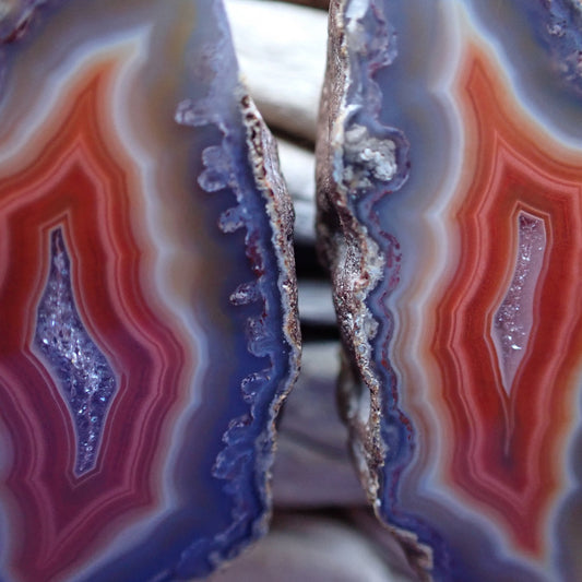 Close-up of a matching Malawi agate cut and hand polished pair. Boasting colorful concentric layers of red, orange, slamon and grey blue with a sparkling druzi centres