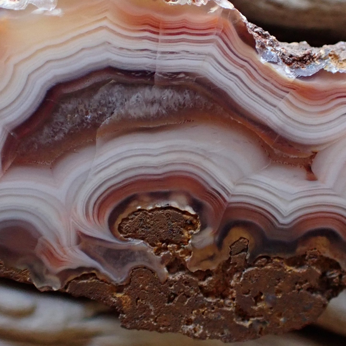 Close-up of a layered Malawi agate stone with pink, bronze and white colors swirling into a gorgeous flow channel