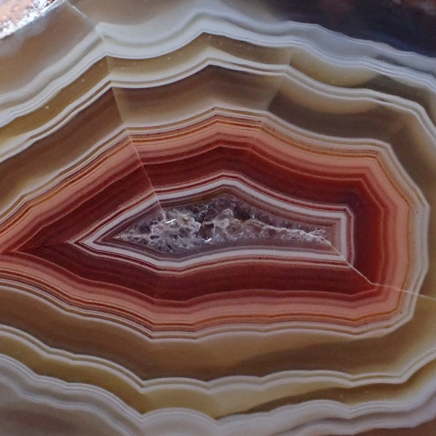 Close-up of the crsyalline centre of a polished Malawi agate sourrounded by bands of deep red and peach fading into rose gold between the outer ghost banding